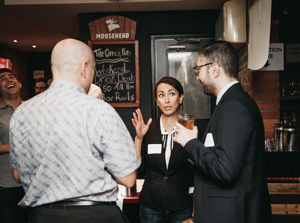 A man holding a beer while a woman speaks to two men